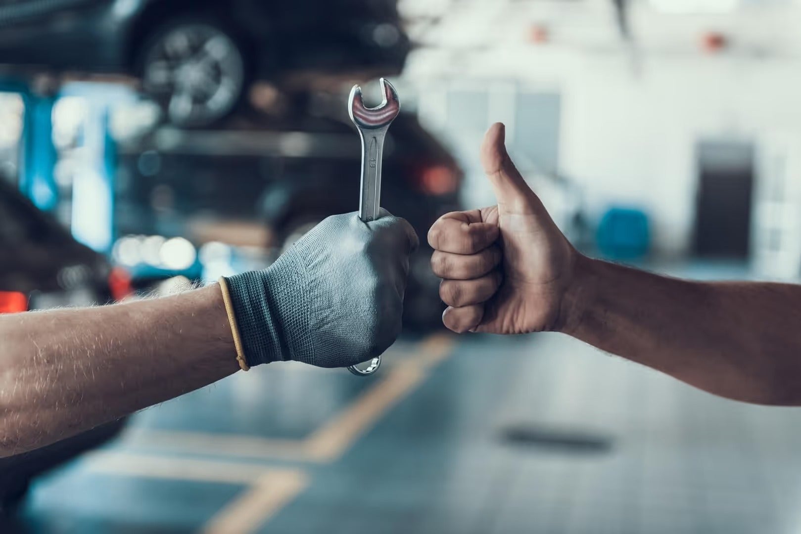Auto service technician giving a thumbs-up while holding a wrench in a service bay